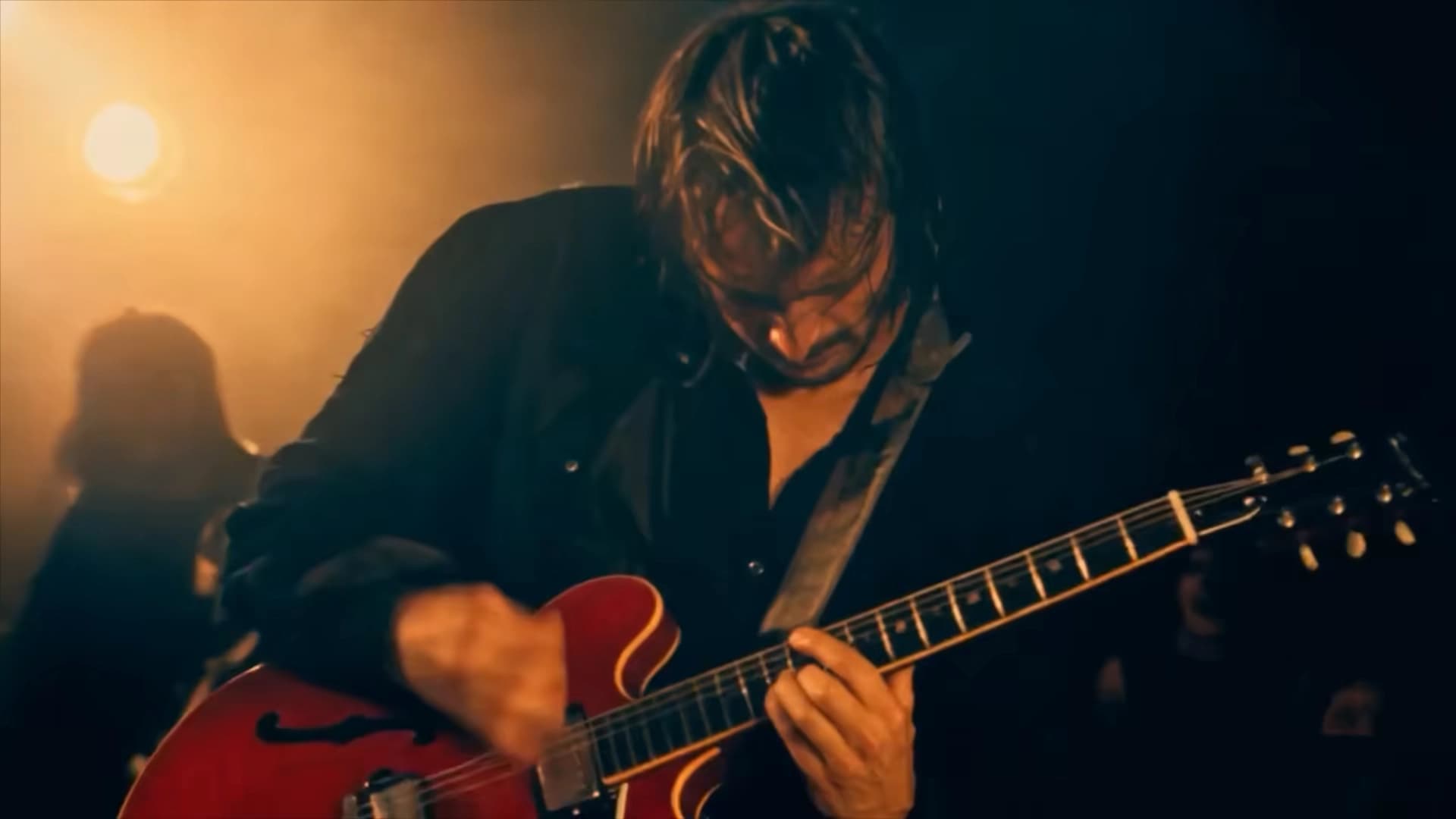Frame from an LTX-2.5 generated clip of a guitarist playing a red hollow-body guitar under warm stage haze