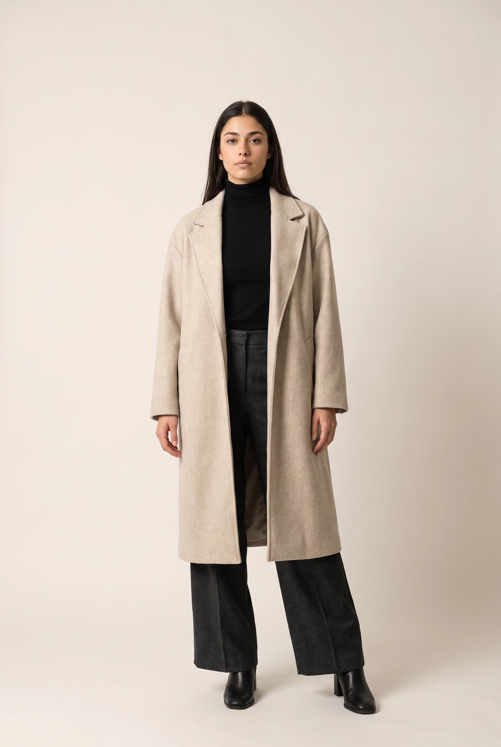 Full-length front-on studio shot of a synthetic model in an open oatmeal wool coat over a black turtleneck and wide-leg charcoal trousers