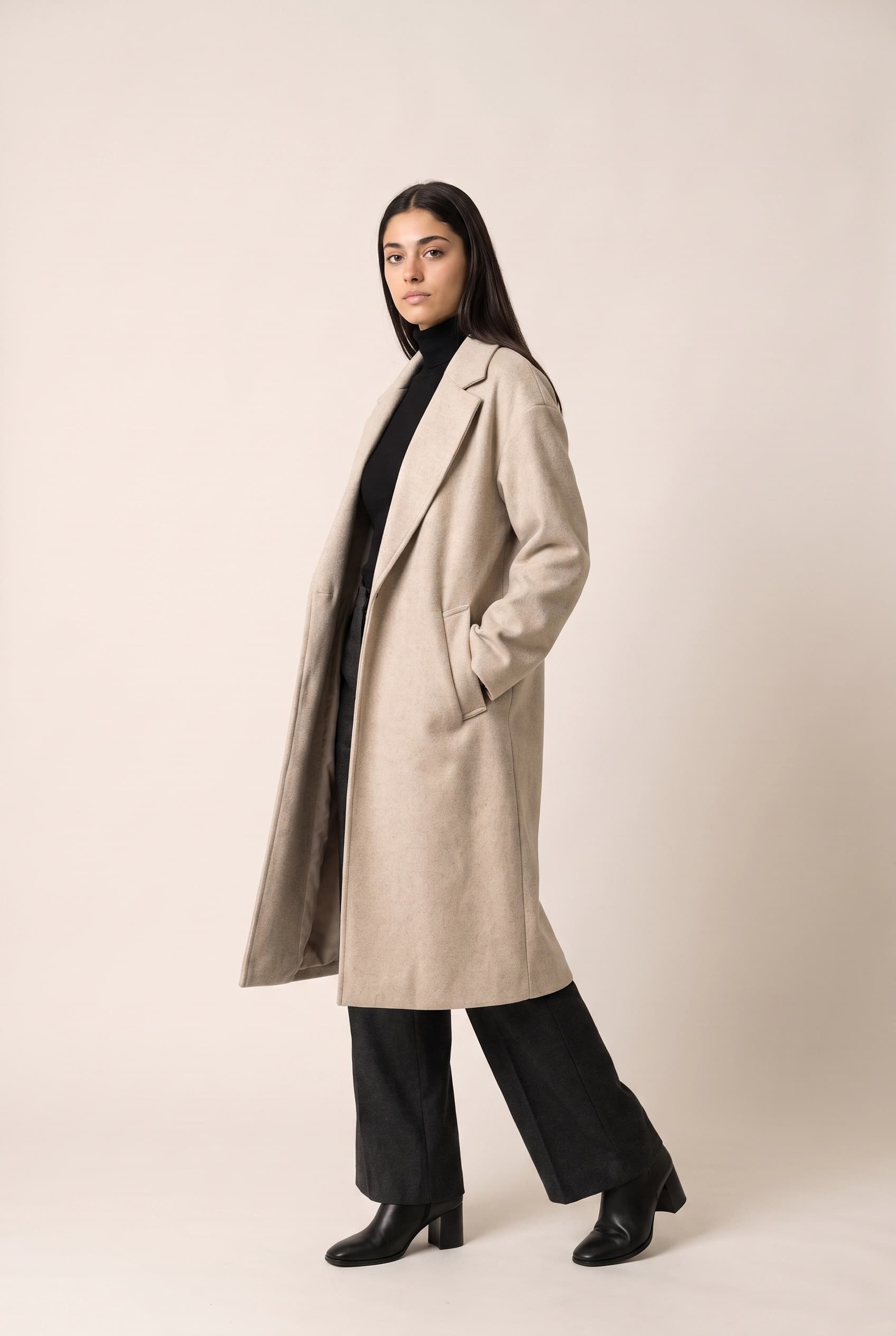 The same model and coat turned three-quarters to camera with one hand in a pocket, showing the drape down the side of the coat