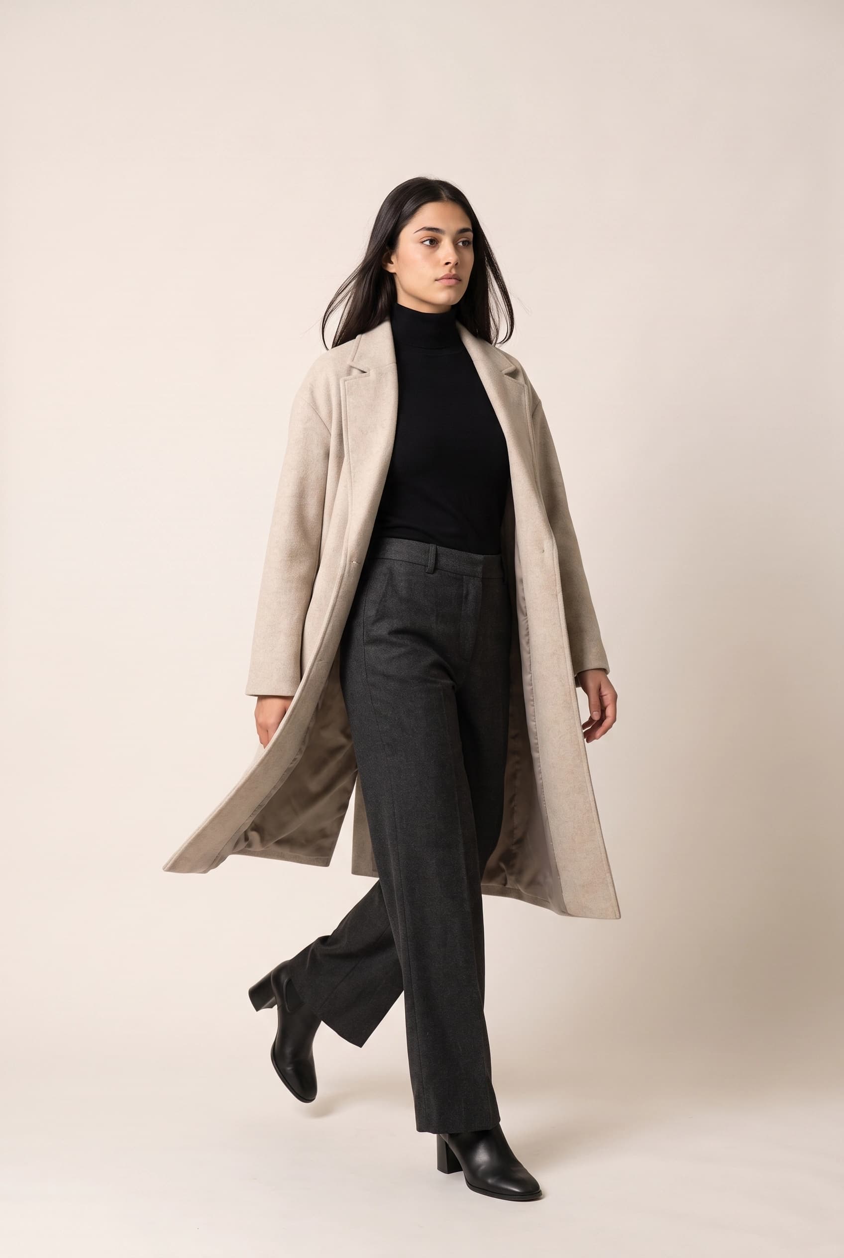 The same model walking toward camera mid-stride, coat swinging open and one boot lifted off the studio floor