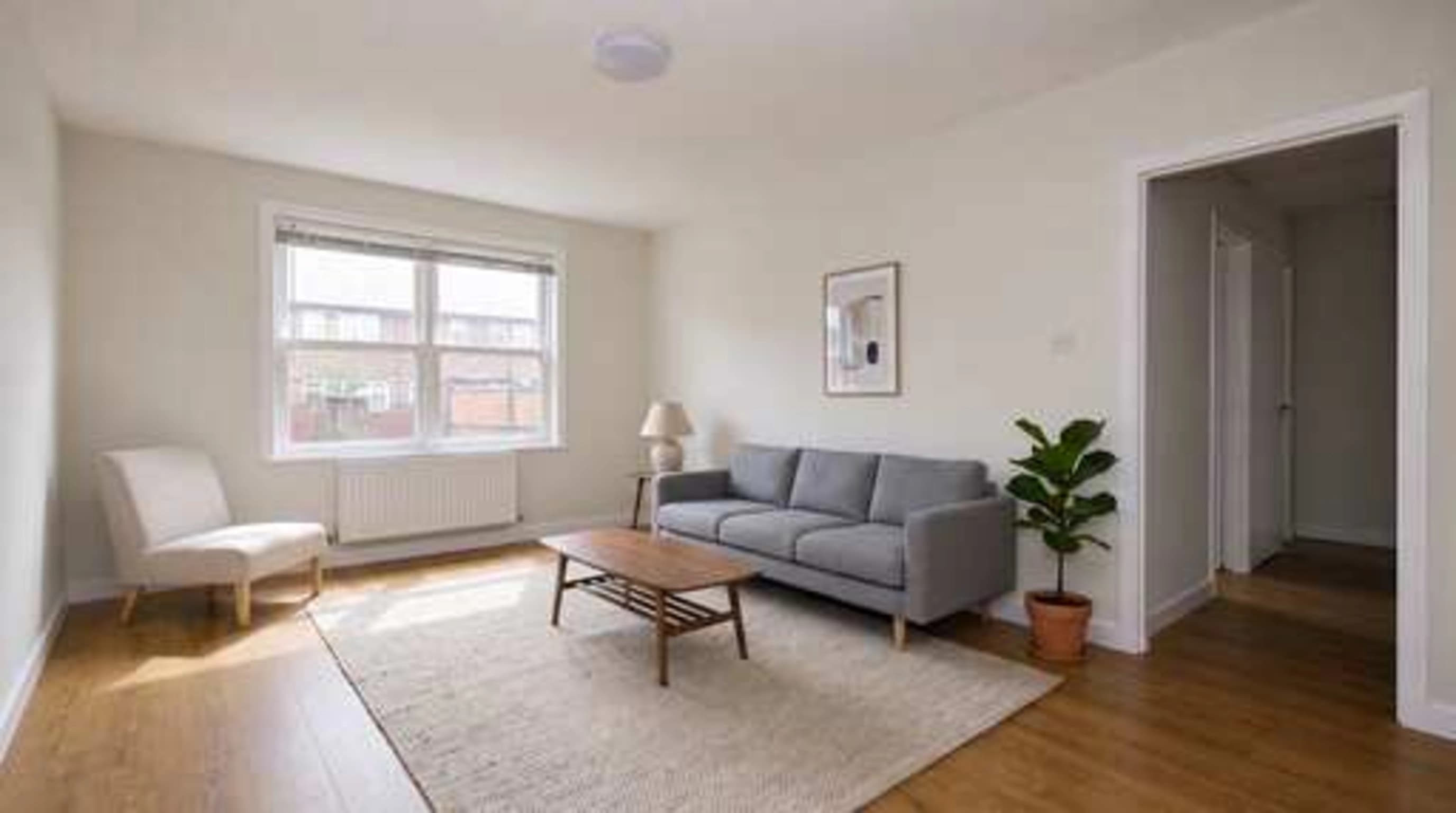 The same staged living room, visibly soft and blocky: the rug weave, window frame and floor grain have smeared into flat patches, with compression artefacts around the sofa edges