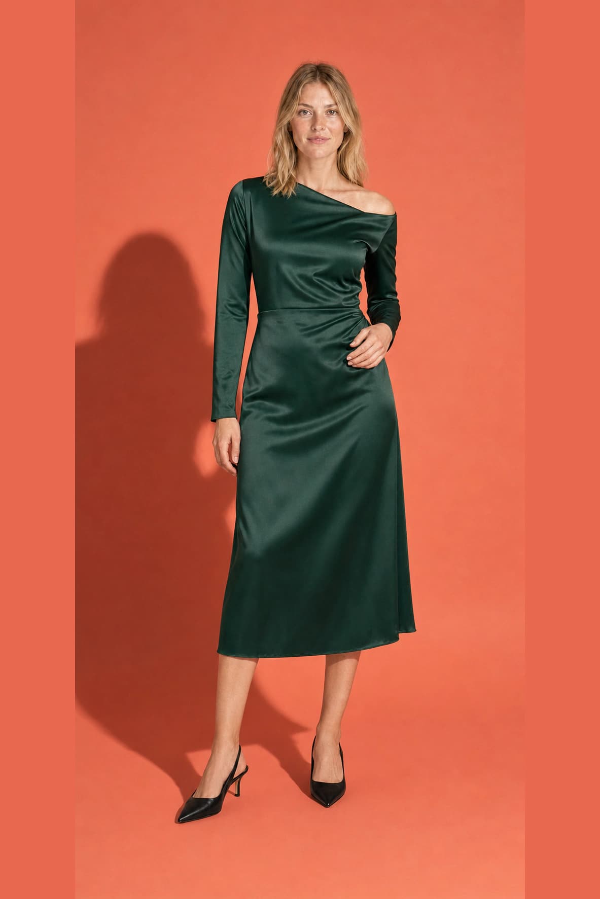 Campaign fashion photograph of the same adult blonde model in a forest-green satin dress