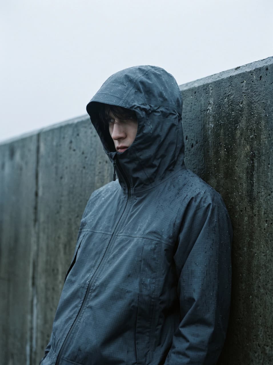 Moodboard tile: model in a graphite ripstop shell jacket against wet concrete under overcast light