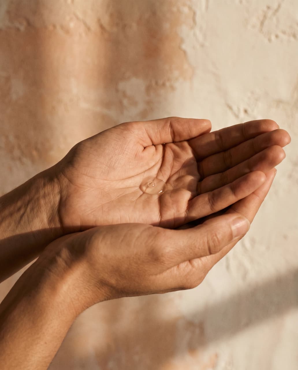 Moodboard tile: cupped hands holding a bead of translucent serum in warm directional light