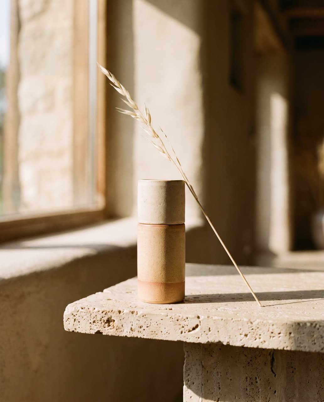 Moodboard tile: matte ceramic serum bottle on a travertine ledge in raking afternoon light